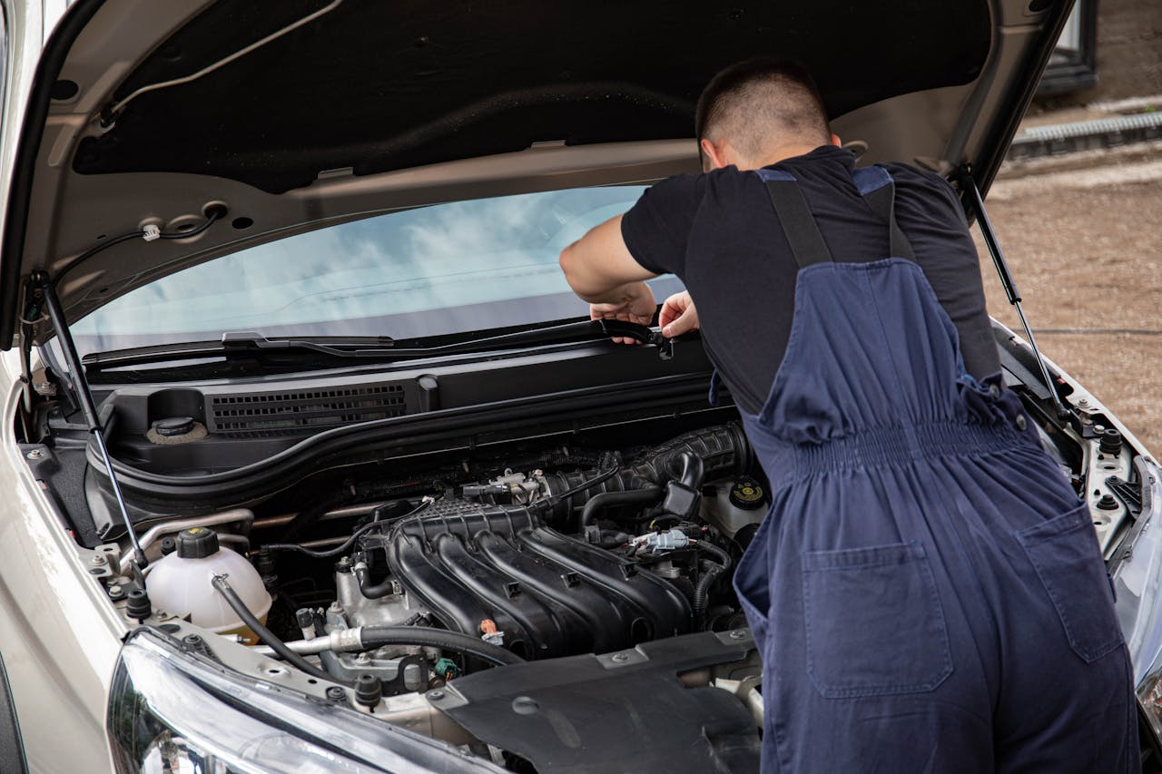 about-us A mechanic in blue overalls working on a car engine as part of maintenance routine.